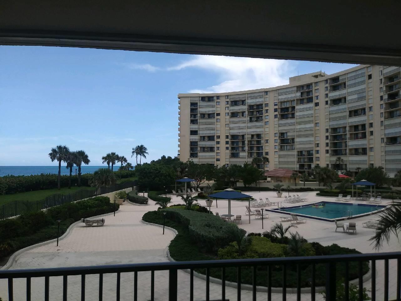 A view from a balcony overlooking a swimming pool, landscaped grounds, and a large building — 200 Ocean Trail Way # 109, Jupiter FL 33477, JUPITER, FL