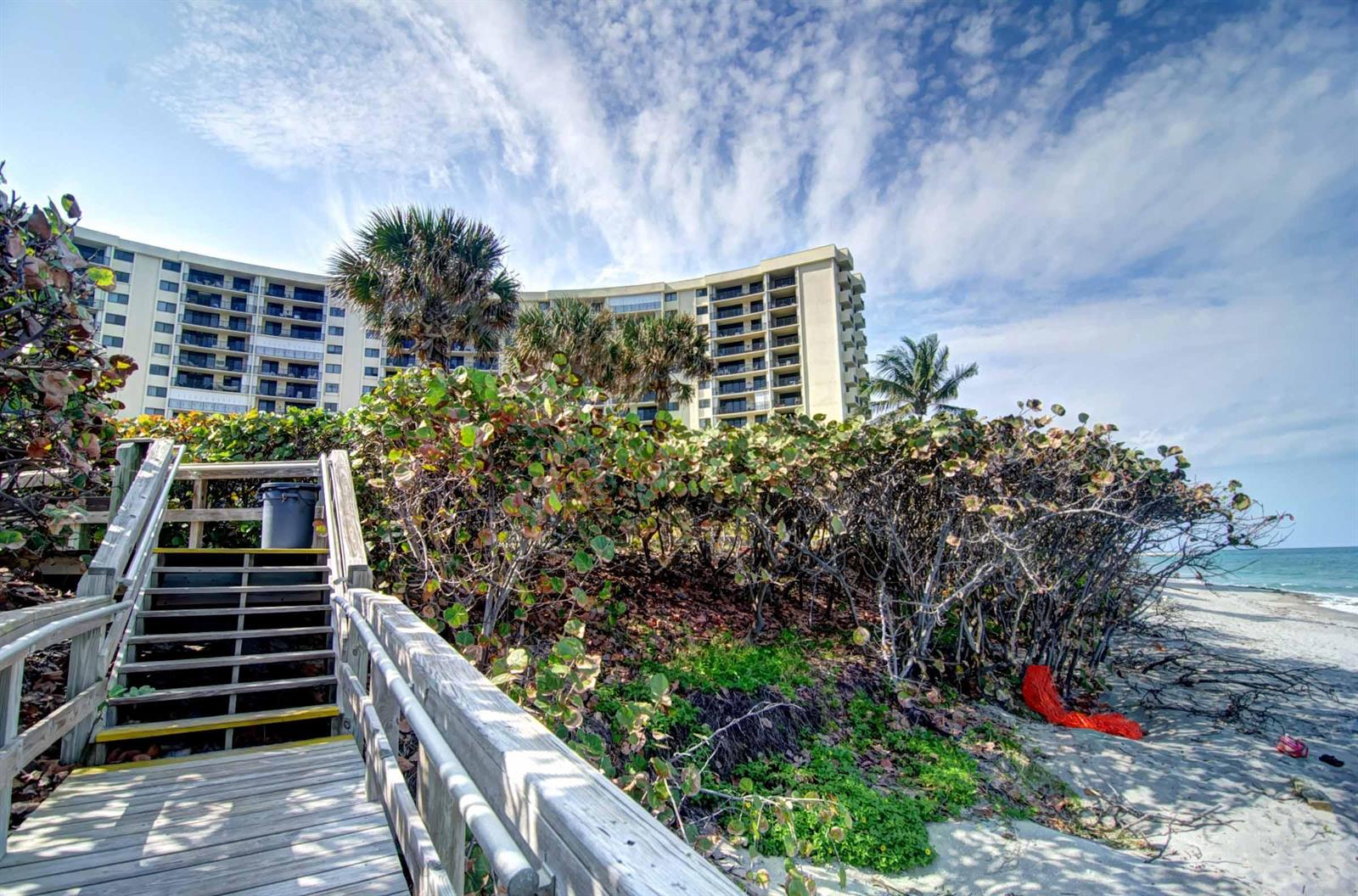 A wooden staircase leads from a sandy beach up toward a large beachfront apartment building — 200 Ocean Trail Way # 109, Jupiter FL 33477, JUPITER, FL