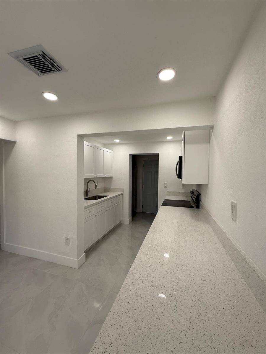 A galley-style kitchen features white cabinets, quartz countertops, and light-colored tile flooring — 4400 SW 36th Street, West Park FL 33023, WEST PARK, FL
