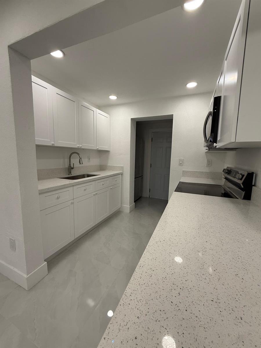 A galley-style kitchen features white cabinets, light countertops, and light-colored tile flooring — 4400 SW 36th Street, West Park FL 33023, WEST PARK, FL