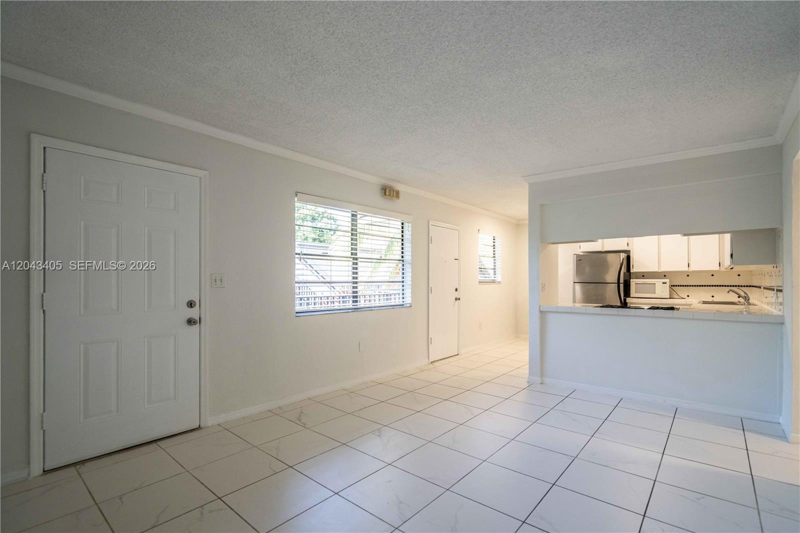 An open-concept living area features white tile flooring, a kitchen pass-through, and two doors — 3265 Virginia St # 18, Miami FL 33133, MIAMI, FL