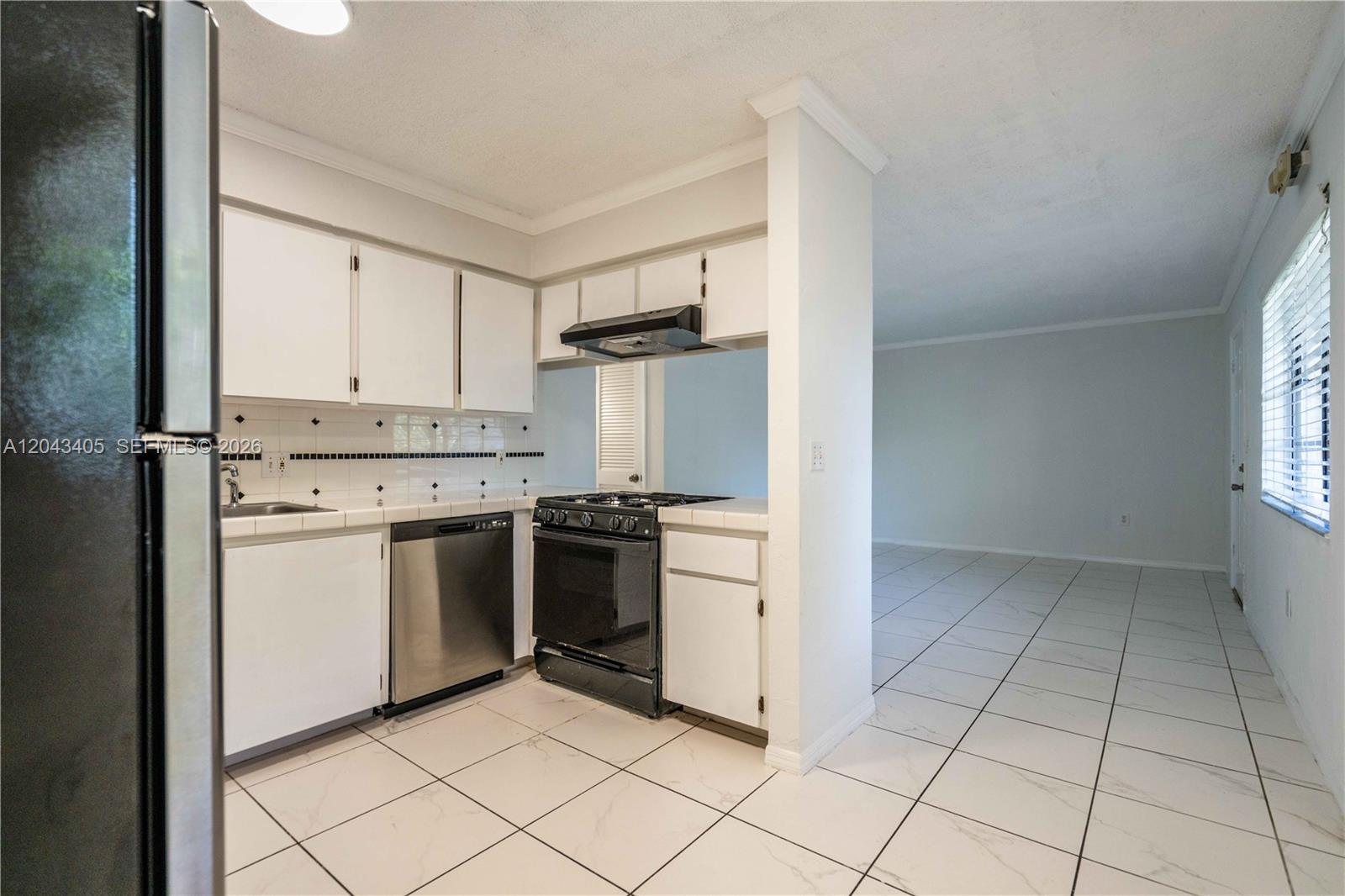 A kitchen with white cabinets, stainless steel appliances, and tiled flooring opens to a room — 3265 Virginia St # 18, Miami FL 33133, MIAMI, FL