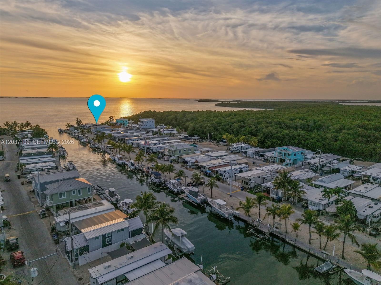 An aerial view shows a canal-side mobile home community at sunset with numerous docked boats — 325 Calusa St, Key Largo FL 33037, KEY LARGO, FL
