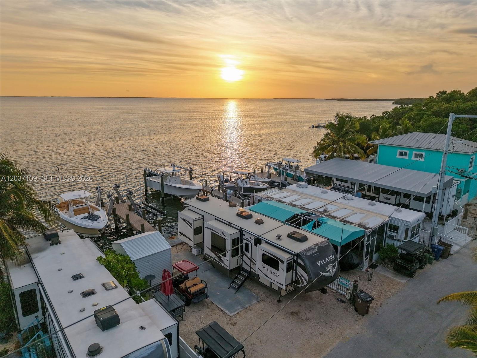 An aerial view shows RVs, boats docked at a pier, and a house at sunset — 325 Calusa St, Key Largo FL 33037, KEY LARGO, FL