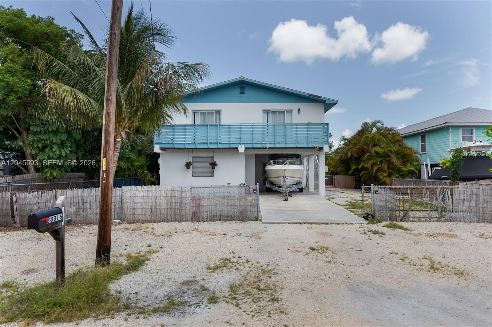 A two-story house with a blue balcony and a boat parked underneath the elevated structure — TORCH KEY, FL
