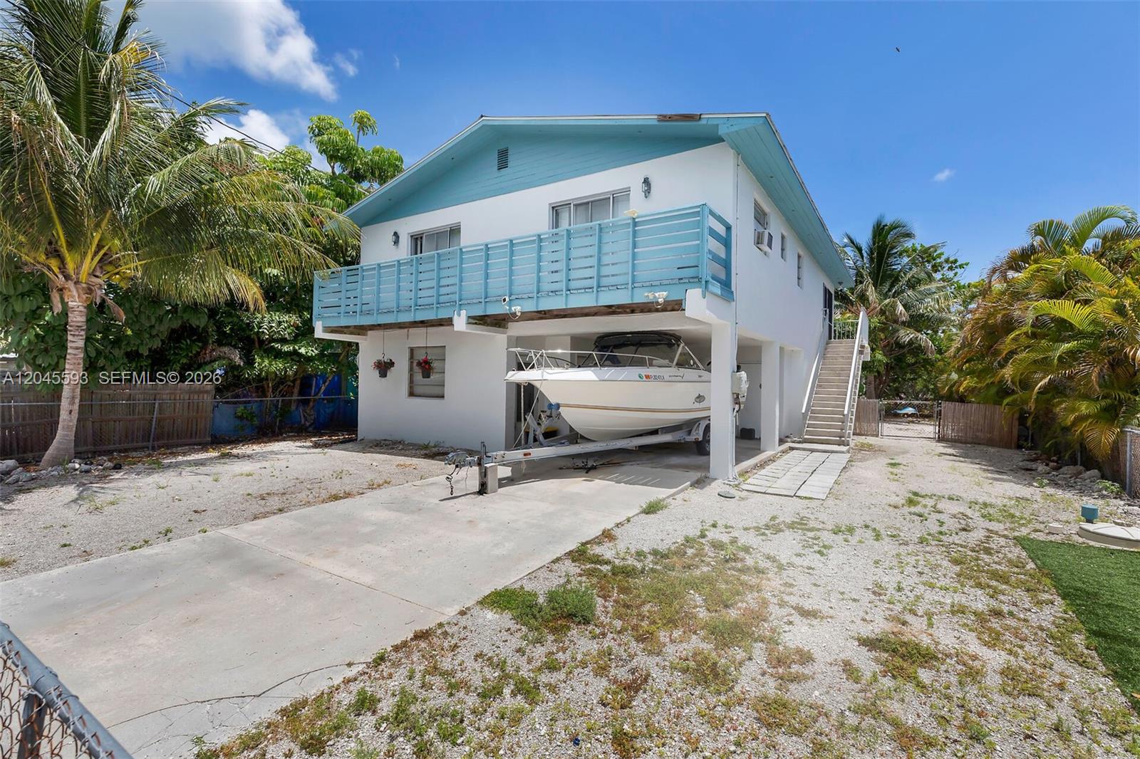 A two-story house with a boat parked underneath the elevated balcony on a gravel lot — TORCH KEY, FL