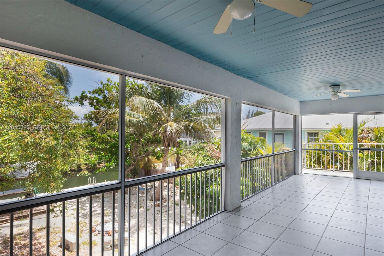 A screened-in balcony features a blue wood-plank ceiling, tiled flooring, and views of a canal — TORCH KEY, FL