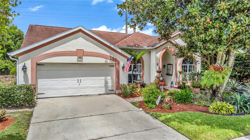 A single-story house with a beige stucco exterior, a two-car garage, and landscaped front yard — 1587 HUNTERS STAND RUN, OVIEDO, FL
