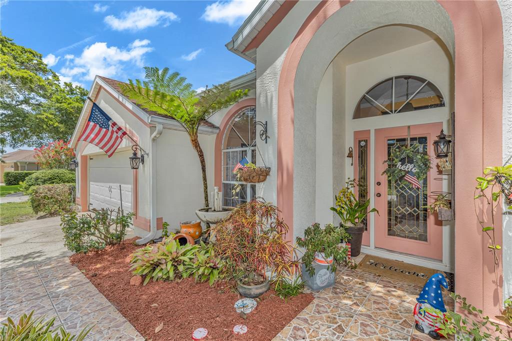 The exterior of a house features a pink-trimmed arched entryway, a front door, and landscaping — 1587 HUNTERS STAND RUN, OVIEDO, FL