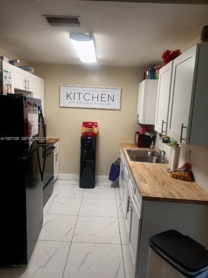 A kitchen features white cabinets, a wood countertop, a black refrigerator, and white tile flooring — 3917 4, Lehigh Acres FL 33971, LEHIGH ACRES, FL