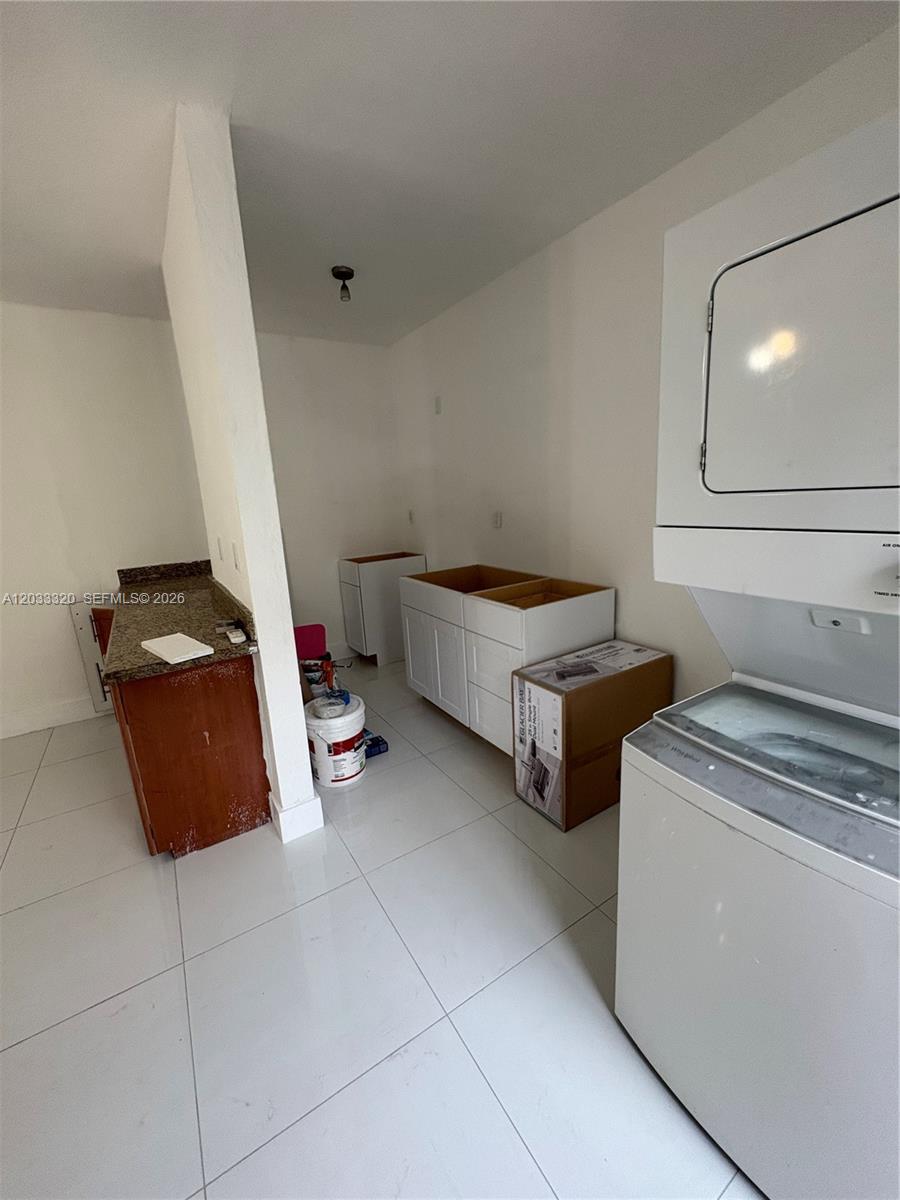 A laundry room features a stacked washer-dryer unit, white base cabinets, and a granite-topped counter — 7920 Harding Ave # 8, Miami Beach FL 33141, MIAMI BEACH, FL