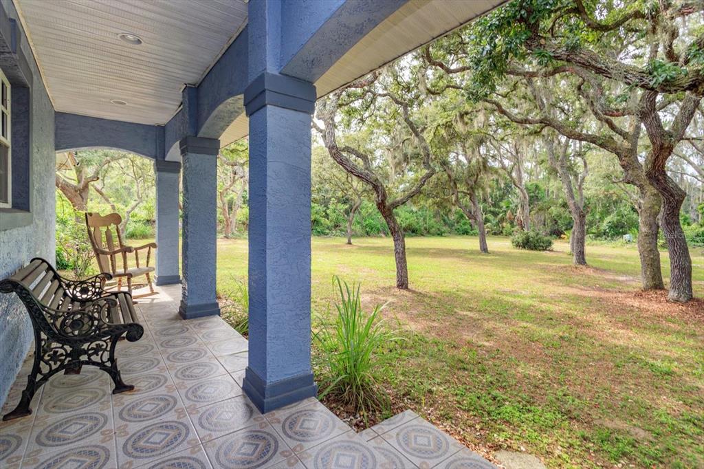 A covered porch with patterned tile flooring overlooks a grassy yard with several large trees — 17249 HOLLY COURT, UMATILLA, FL
