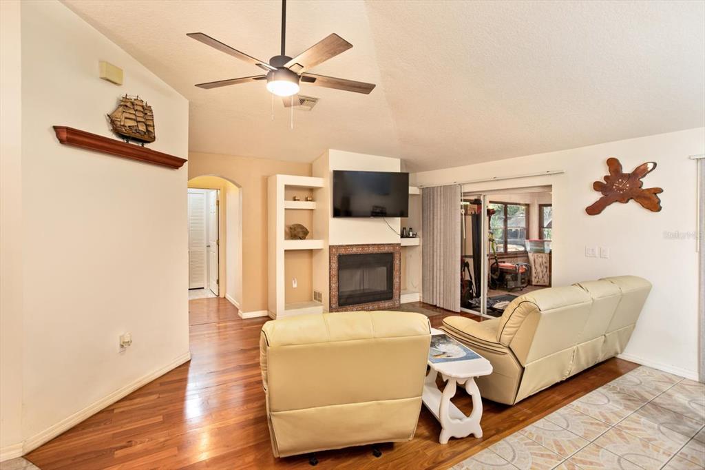 A living room features a fireplace, television, ceiling fan, and a mix of wood and tile flooring — 17249 HOLLY COURT, UMATILLA, FL