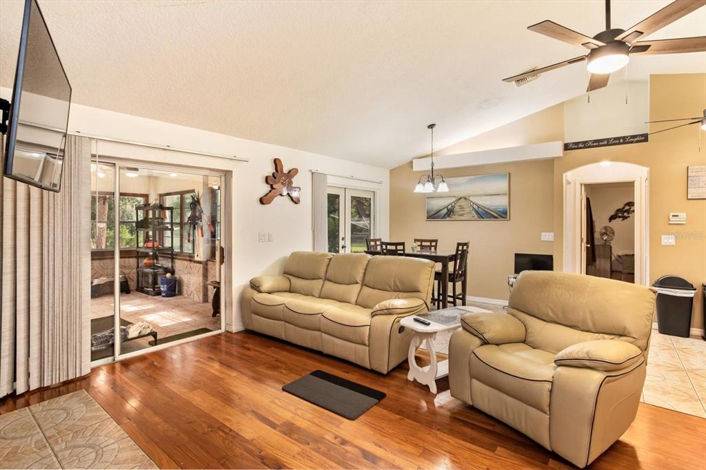 A living room with hardwood floors, a tan sofa and armchair, and a sliding glass door — 17249 HOLLY COURT, UMATILLA, FL