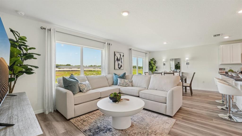 A bright living room features a large sectional sofa, a round coffee table, and wood-look flooring — 1118 WILD CLOVER WAY, PLANT CITY, FL