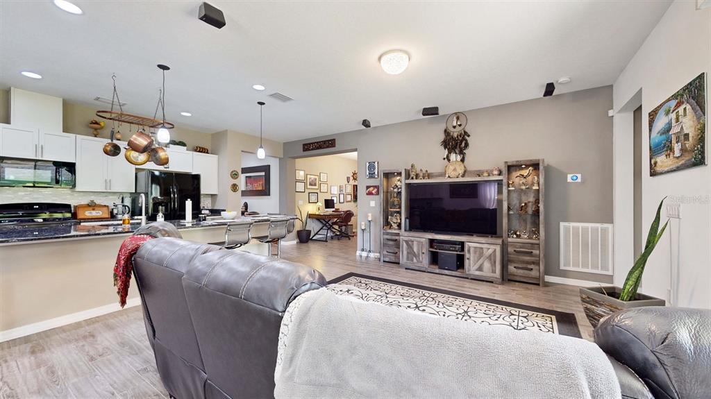 An open-concept living room and kitchen feature gray wood-look flooring and a large entertainment center — 626 CONSERVATION BOULEVARD, GROVELAND, FL