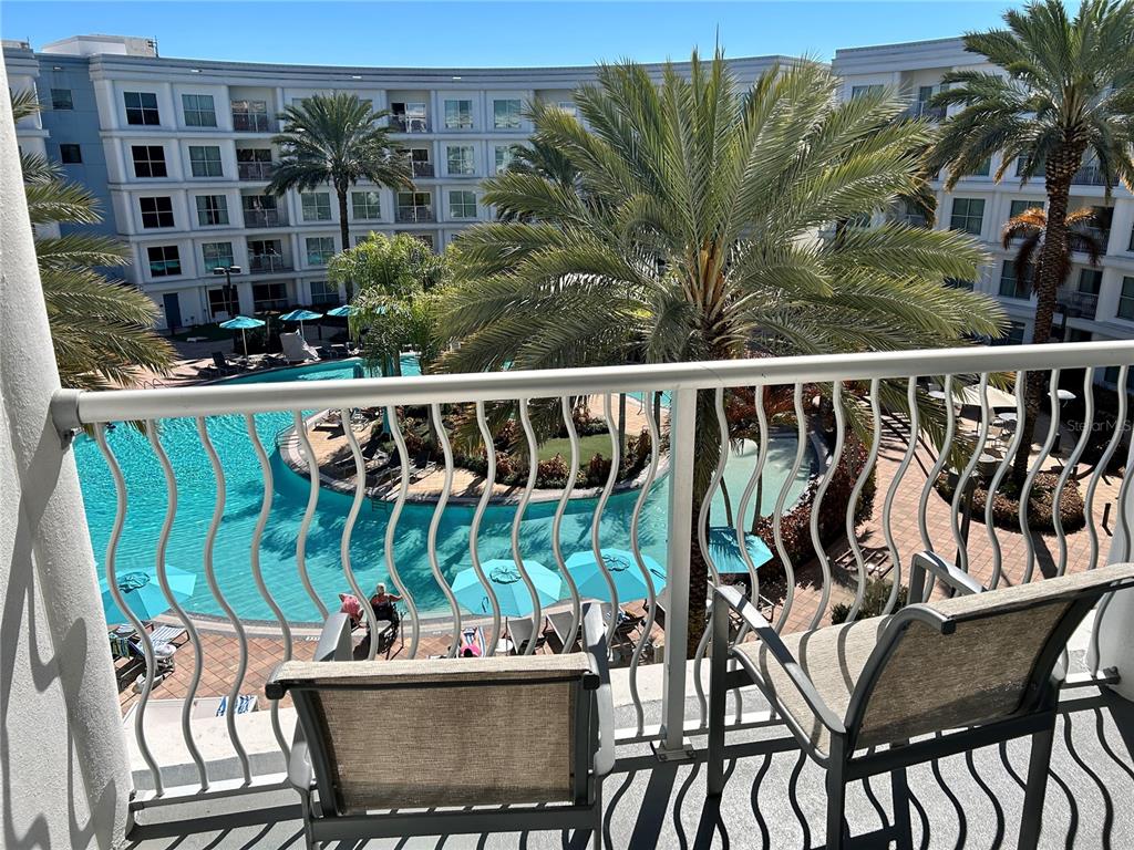 A balcony view overlooks a swimming pool surrounded by palm trees and a multi-story building — 225 CELEBRATION PLACE UNIT 446, KISSIMMEE, FL