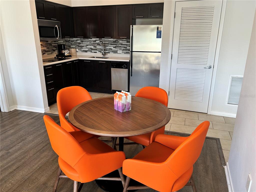 A kitchen with dark cabinets and stainless steel appliances sits behind a round dining table — 225 CELEBRATION PLACE UNIT 446, KISSIMMEE, FL