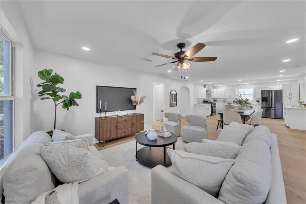 A bright, open-concept living room features light-colored sofas, a wooden media console, and a kitchen — 1110 12TH STREET N, ST PETERSBURG, FL