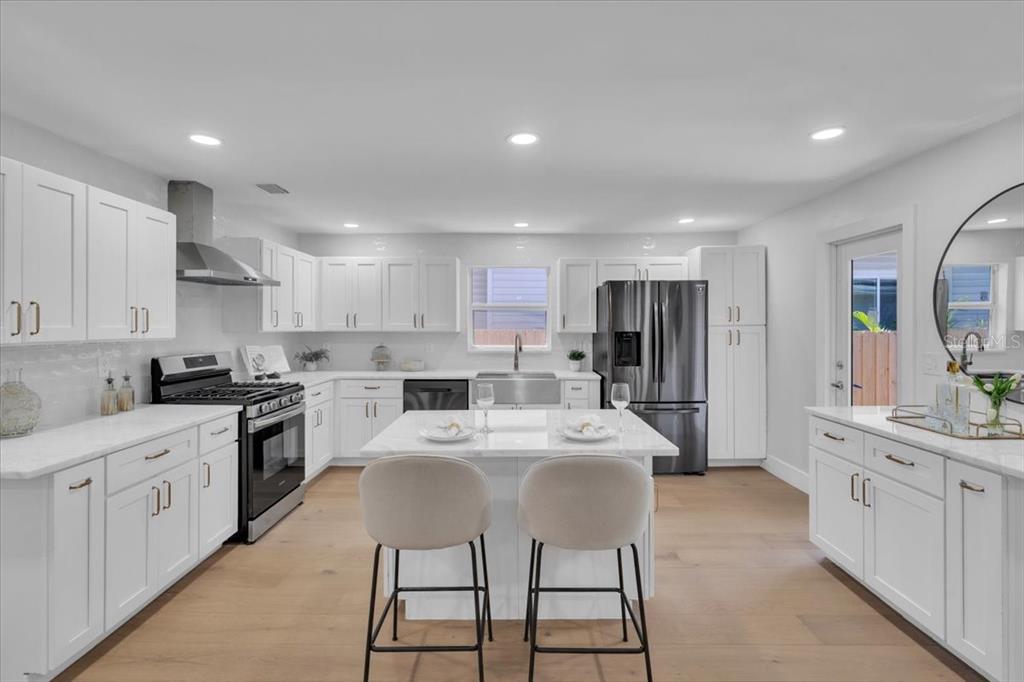 A modern white kitchen features a central island, stainless steel appliances, and light wood flooring — 1110 12TH STREET N, ST PETERSBURG, FL
