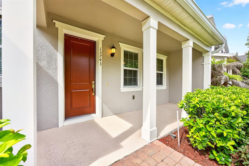A covered front porch features a red door, white columns, and a small light fixture — 13743 CALERA ALLEY, WINDERMERE, FL