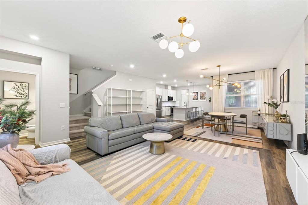 An open-concept living and dining area features a gray sectional, modern lighting, and wood flooring — 13743 CALERA ALLEY, WINDERMERE, FL