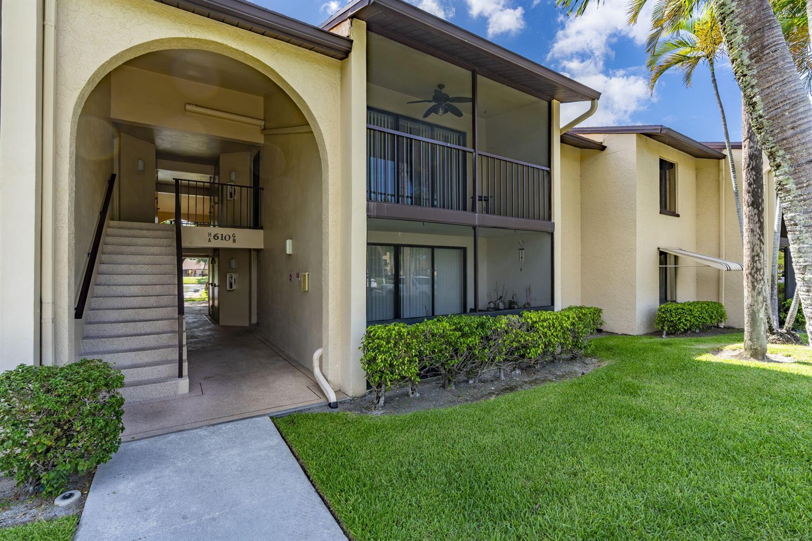 A two-story apartment building features a covered staircase, screened balconies, and a manicured lawn — 610 Sea Pine Way # B2, FL 33415, FL