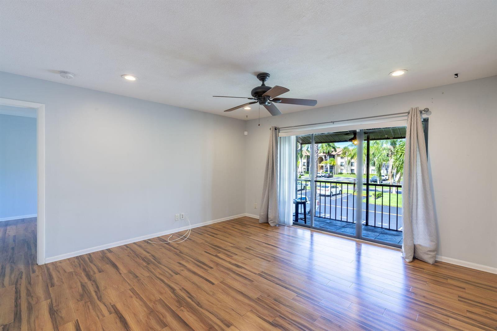 An empty living room features light gray walls, wood-look flooring, a ceiling fan, and a balcony — 610 Sea Pine Way # B2, FL 33415, FL
