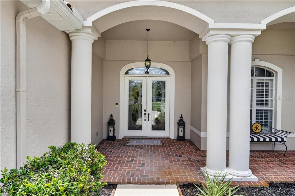 A covered brick entryway features double glass doors flanked by white columns and lanterns — 3874 CRESCENT COVE PLACE, TARPON SPRINGS, FL