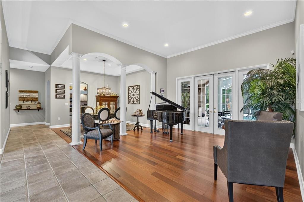 A living area with hardwood floors, a grand piano, and white columns separating the space — 3874 CRESCENT COVE PLACE, TARPON SPRINGS, FL
