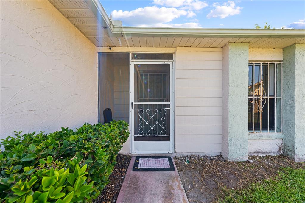 A house exterior features a screened front door, a window with security bars, and landscaping — 743 DROMEDARY DRIVE, POINCIANA, FL