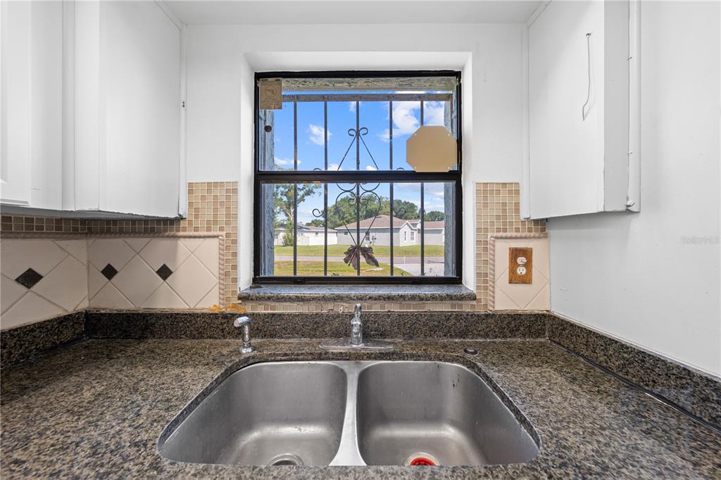 A kitchen sink with granite countertops and a window featuring security bars — 743 DROMEDARY DRIVE, POINCIANA, FL
