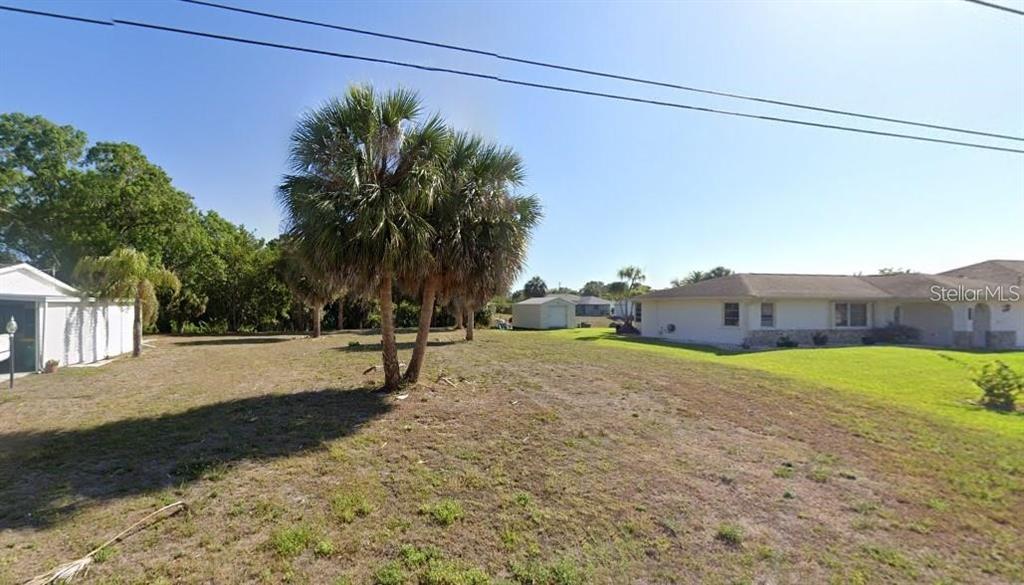 A grassy lot features a palm tree in the foreground and neighboring houses nearby — 2272 AUBURN BOULEVARD, PORT CHARLOTTE, FL