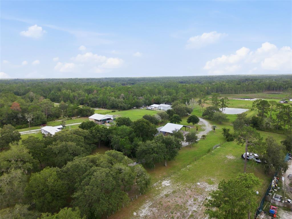 An aerial view shows several buildings, trees, and a pond on a large rural property — 32402 PINE ROAD, EUSTIS, FL