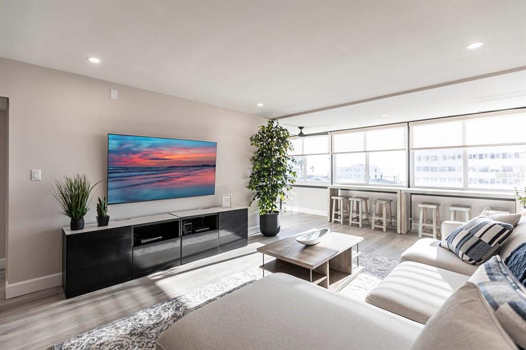 A modern living room features a large television, a sectional sofa, and window-side bar seating — 1125 W PEPPERTREE DRIVE UNIT 402, SARASOTA, FL