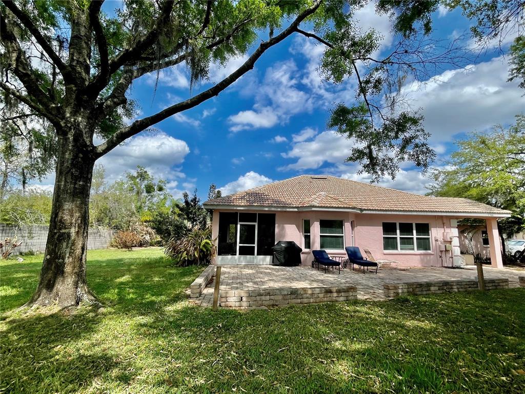 A pink house with a tiled roof and a brick patio sits under large trees — 21007 LOS CABOS COURT, LAND O LAKES, FL
