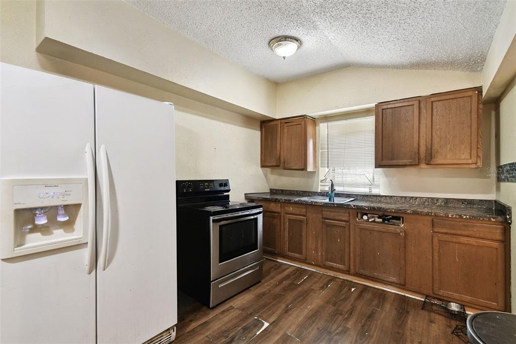 A kitchen features wood cabinets, dark countertops, a black stove, and a white refrigerator — 3417 E LAKE AVENUE, TAMPA, FL