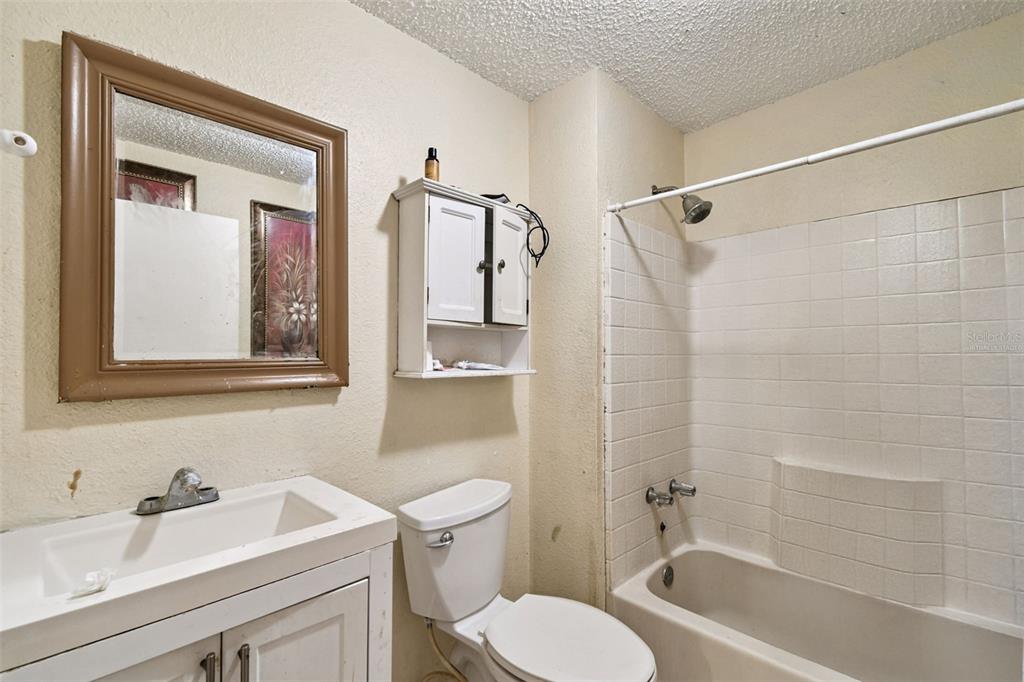 A bathroom features a white vanity, a toilet, and a shower-tub combination with white tiles — 3417 E LAKE AVENUE, TAMPA, FL