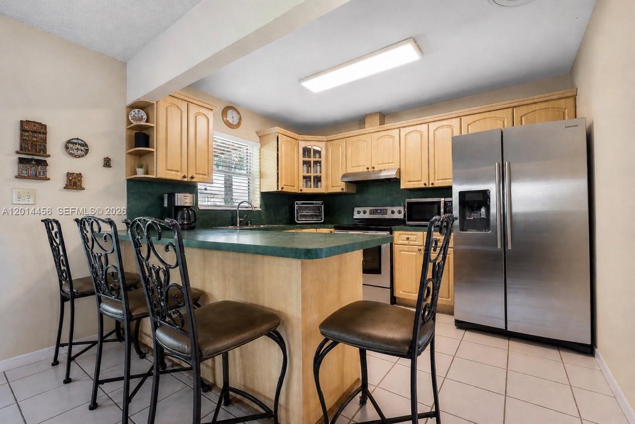 A kitchen features light wood cabinets, a green countertop, stainless steel appliances, and four chairs — 10315 SW 26th Ter, Miami FL 33165, MIAMI, FL