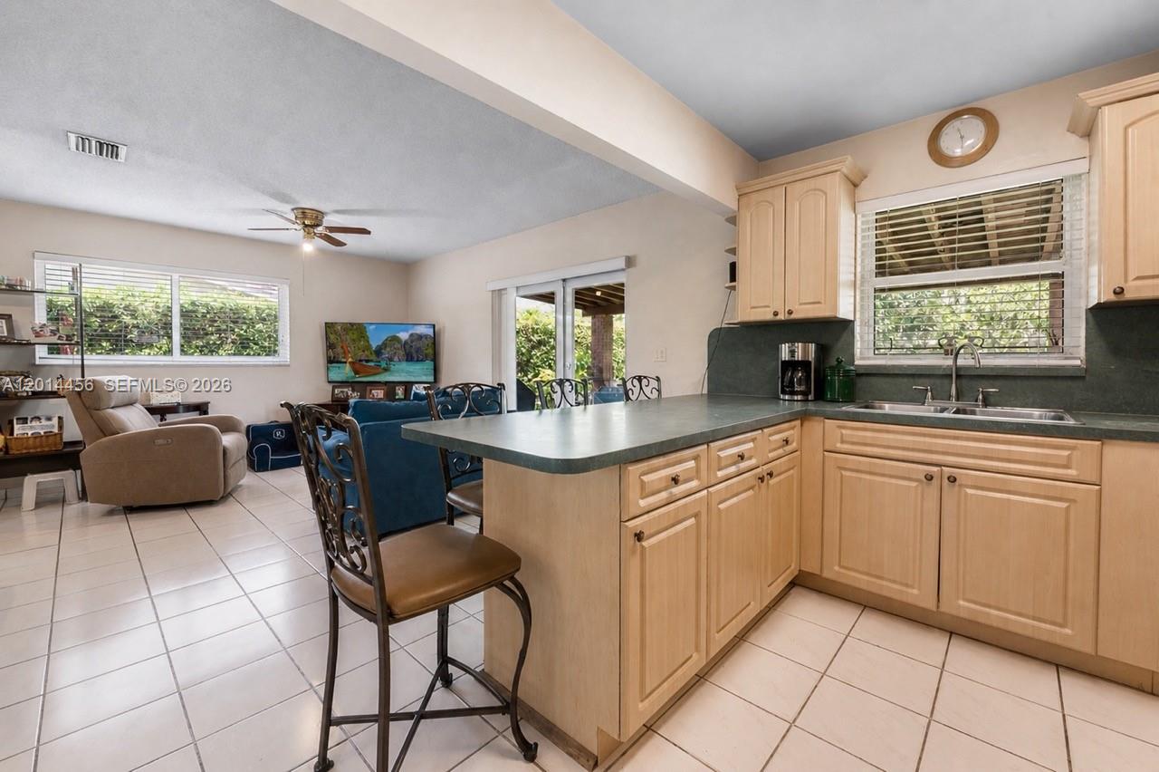 A kitchen with light wood cabinets and a green countertop overlooks a living area — 10315 SW 26th Ter, Miami FL 33165, MIAMI, FL