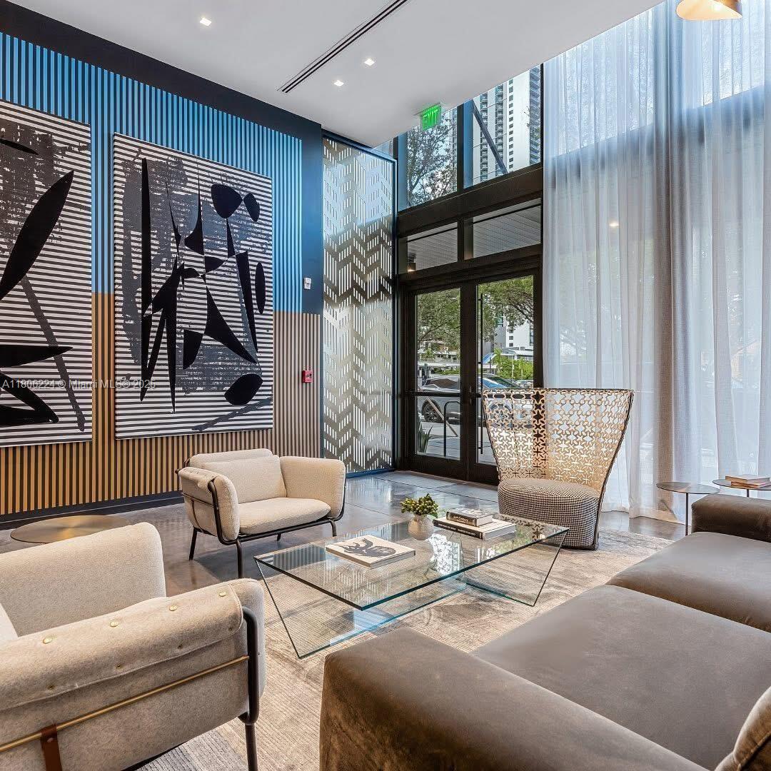 A modern lobby features tall windows, abstract wall art, and contemporary seating around a glass table — 398 NE 5th St # 1619, Miami FL 33132, MIAMI, FL