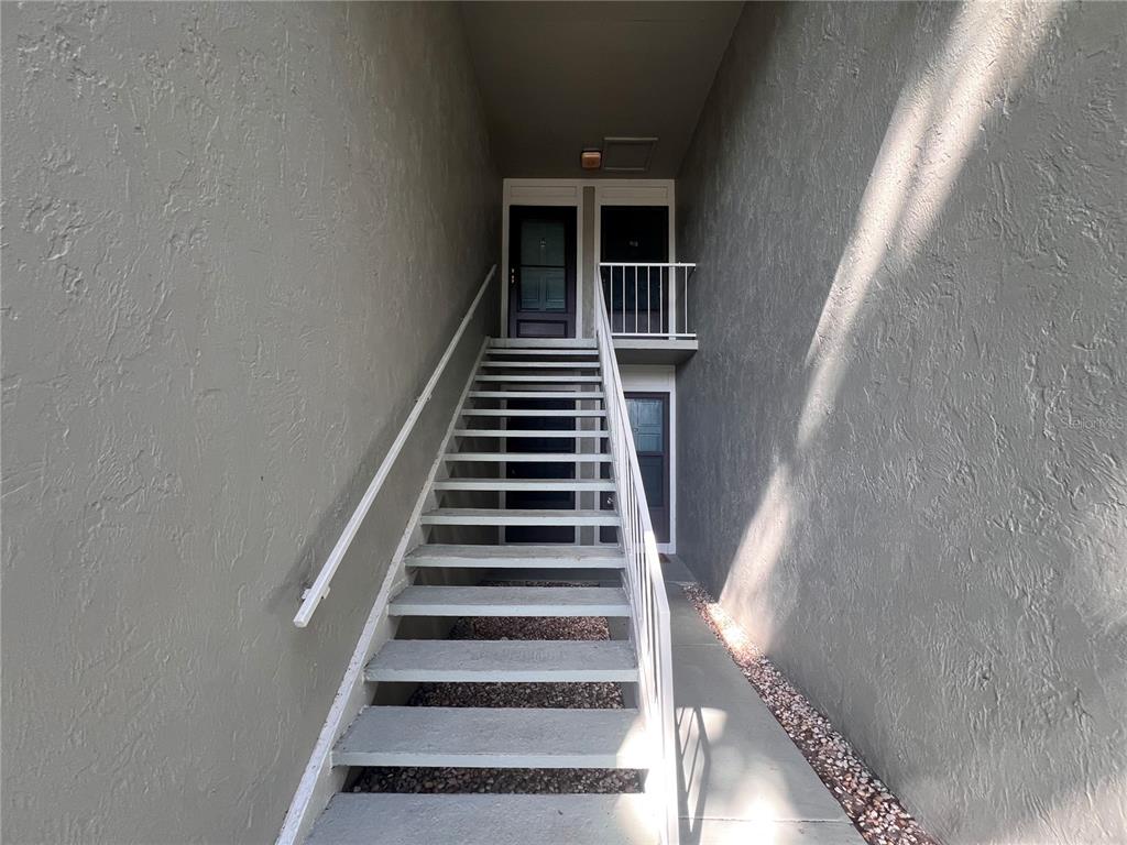 An exterior staircase leads to two levels of apartment entry doors between two stucco walls — 302 PALM COAST PARKWAY NE UNIT 204, PALM COAST, FL