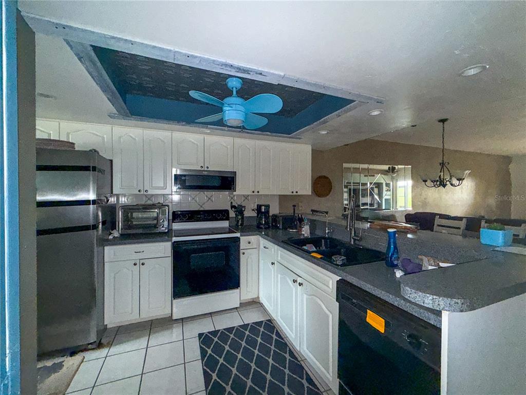 A kitchen features white cabinets, stainless steel appliances, a dark countertop, and a blue ceiling fan — 6800 PLACIDA ROAD UNIT 144, ENGLEWOOD, FL