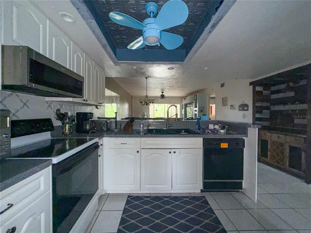 A kitchen features white cabinets, dark countertops, a blue ceiling fan, and tiled flooring — 6800 PLACIDA ROAD UNIT 144, ENGLEWOOD, FL