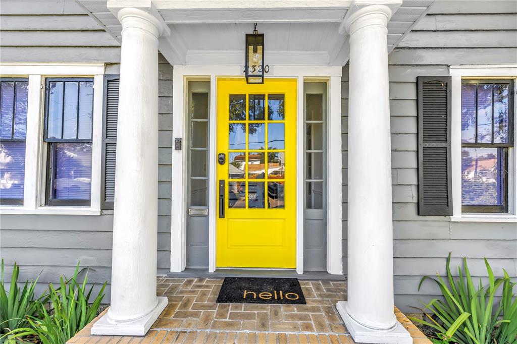 A bright yellow front door with glass panes sits between two white columns on a porch — 2320 5TH STREET N, ST PETERSBURG, FL