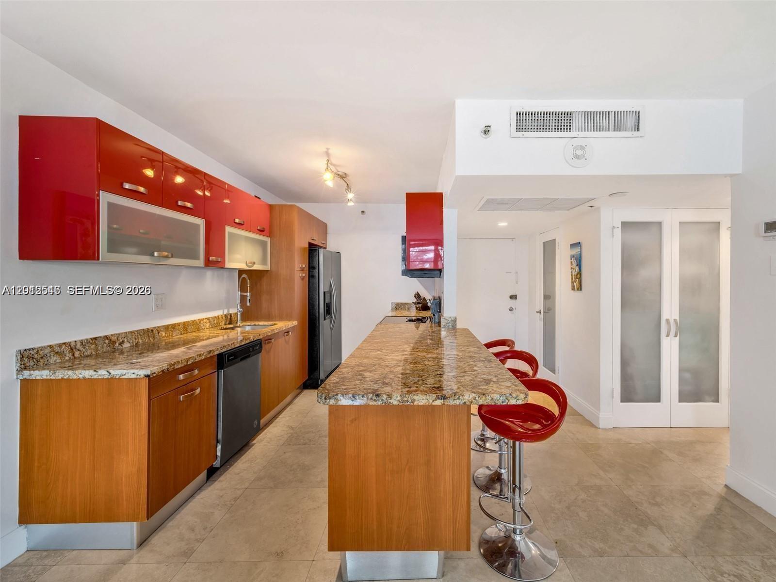 A kitchen features wood cabinets, red upper cabinets, granite countertops, and a breakfast bar — 100 Lincoln Rd # 308, Miami Beach FL 33139, MIAMI BEACH, FL