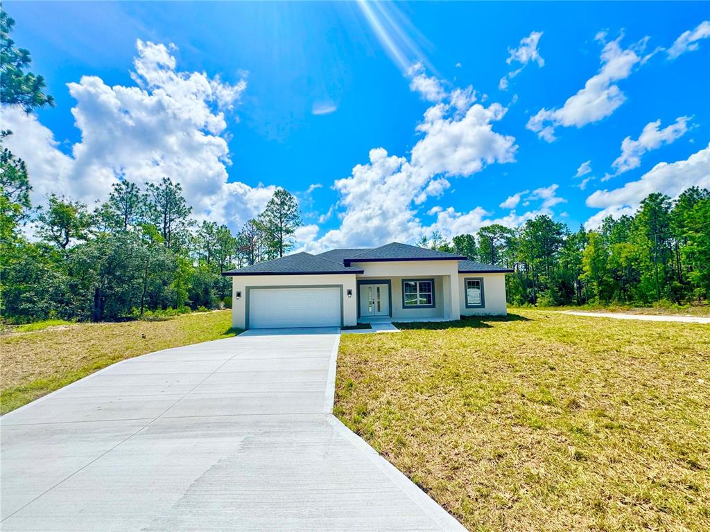 A single-story house with a white garage and concrete driveway sits on a grassy lot — 9835 N ESSEX TERRACE, DUNNELLON, FL