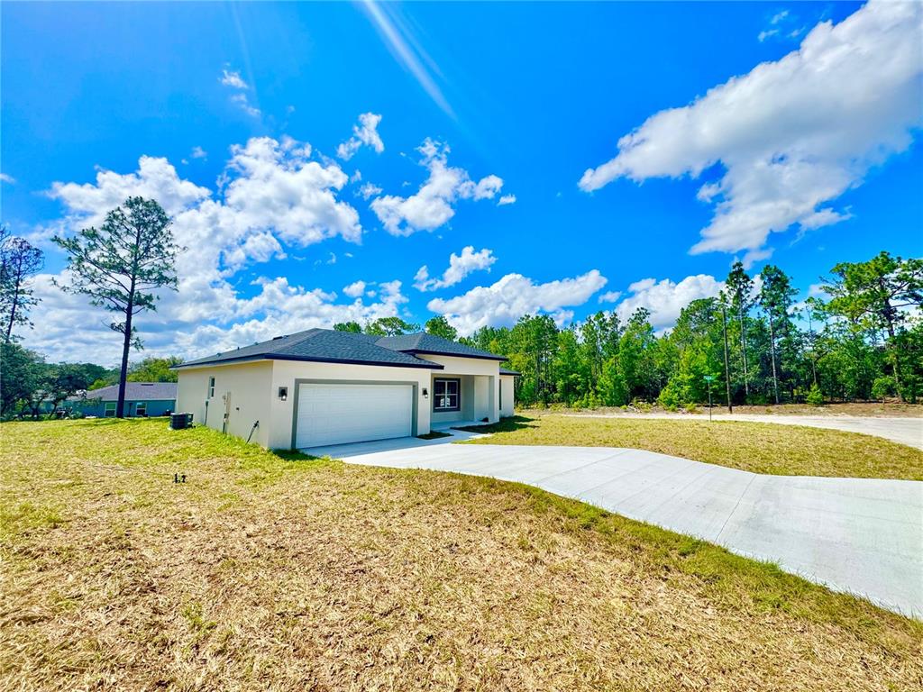 A single-story house with a white garage and a concrete driveway under a blue sky — 9835 N ESSEX TERRACE, DUNNELLON, FL