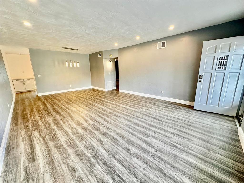 An empty living room features gray wood-look flooring, recessed lighting, and a white front door — 2431 CANADIAN WAY UNIT 37, CLEARWATER, FL