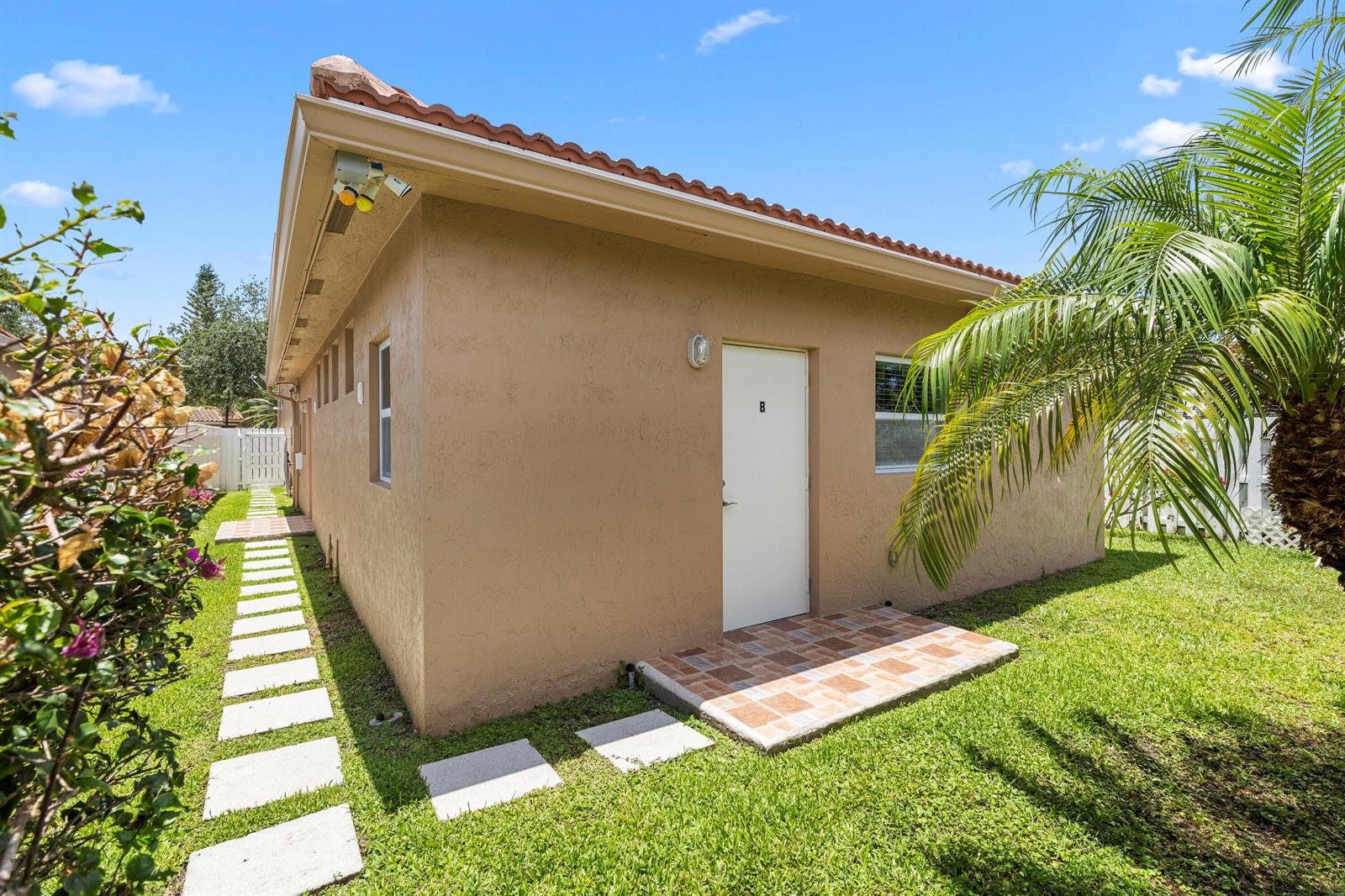 A tan stucco exterior of a small building with a white door labeled B — 907 Stanton Drive, Weston FL 33326, WESTON, FL